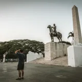 A man stands near a historic statue and obelisk in a plaza in Caracas, Venezuela.
