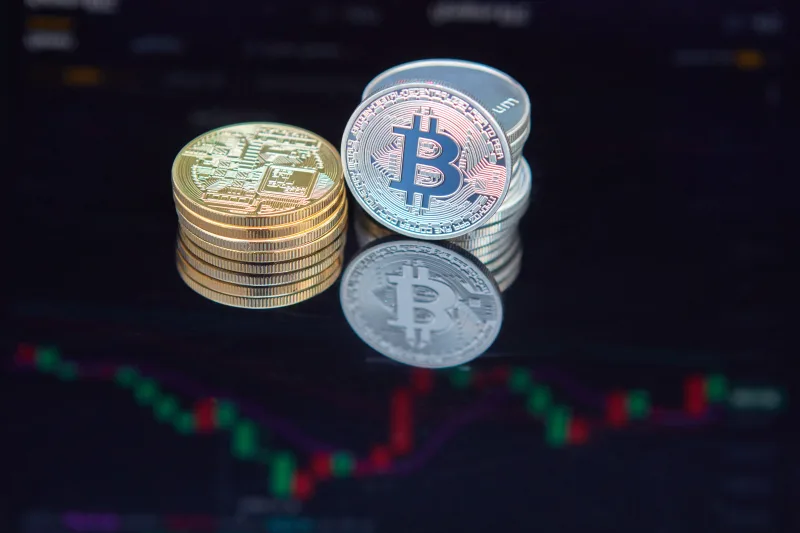 Close-up of bitcoin coins reflecting on a screen with financial market data, highlighting digital currency trend.