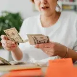 A woman sits indoors counting cash at her office desk, focusing on finances.