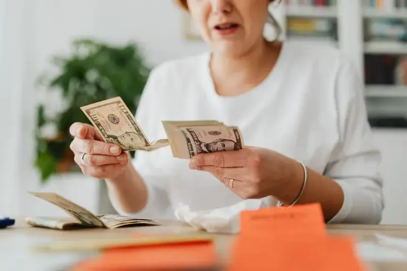 A woman sits indoors counting cash at her office desk, focusing on finances.