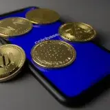 Five cryptocurrency coins displayed on a smartphone with Coinbase app open.