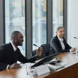 Two professionals speaking at a business conference in a modern office setting.