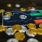 Bitcoin and altcoins on table with digital trading chart indicating market trends and investment details.