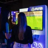 Two women playing FIFA on a PlayStation 5 console in a modern gaming store.