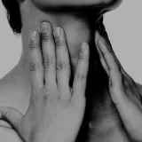 A close up of a person feeling their neck with both hands
