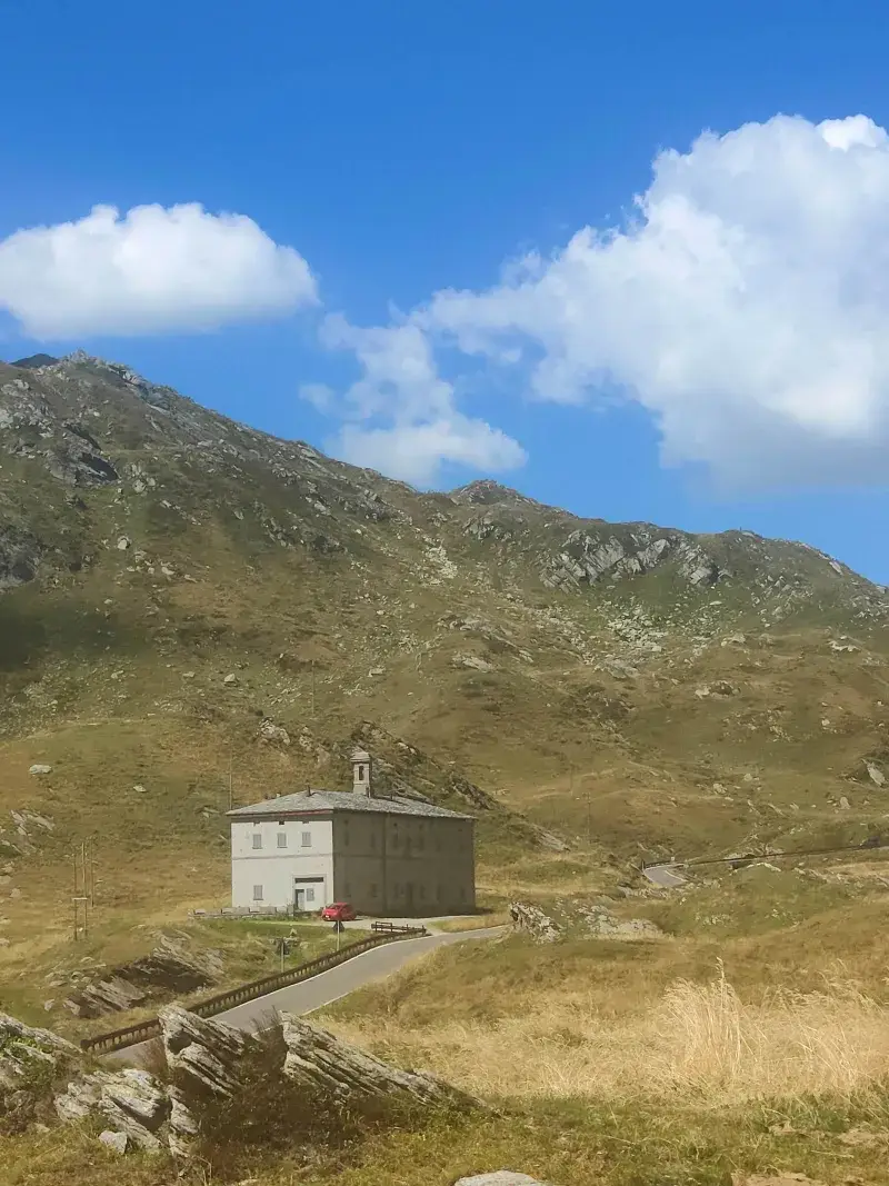 A remote building on San Bernardino Pass amidst mountainous terrain under a clear blue sky.
