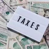 From above of white retro lightbox with TAXES inscription placed on pile of USA dollar bills on white surface