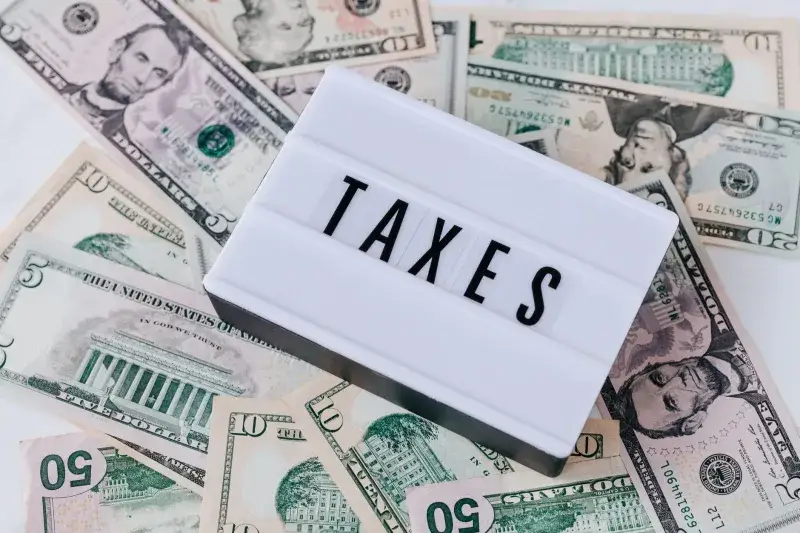 From above of white retro lightbox with TAXES inscription placed on pile of USA dollar bills on white surface