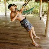 Fit man performing TRX workout on a wooden deck with tropical backdrop, showcasing outdoor exercise and healthy lifestyle.