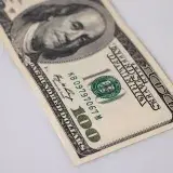 Detailed close-up of a one hundred dollar US bill on a white surface.