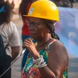A black woman wearing a helmet and sundress speaks into a microphone during a street protest.