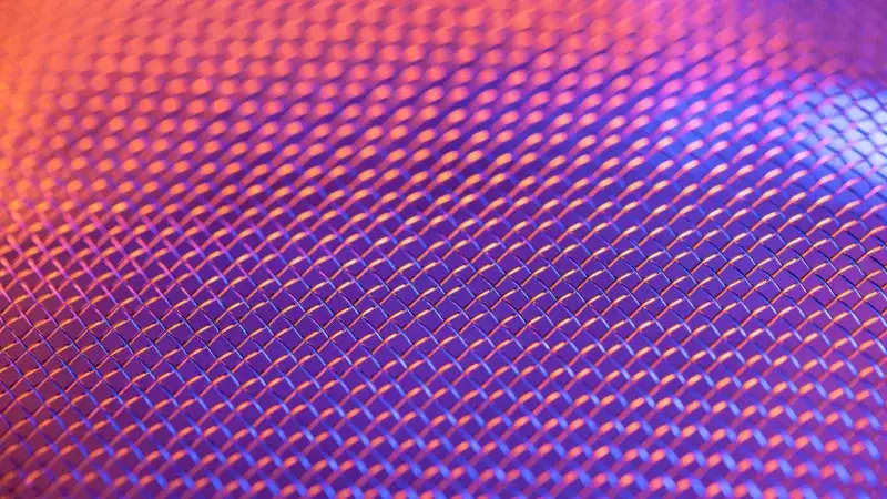 Close-up of a metallic mesh pattern with vibrant lighting creating a colorful abstract effect.