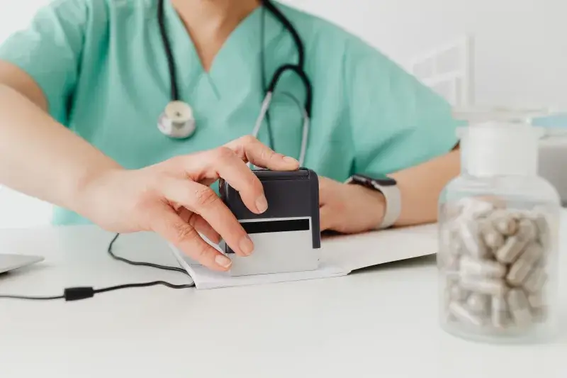 Close-up of a doctor stamping a prescription with a bottle of pills on a desk.