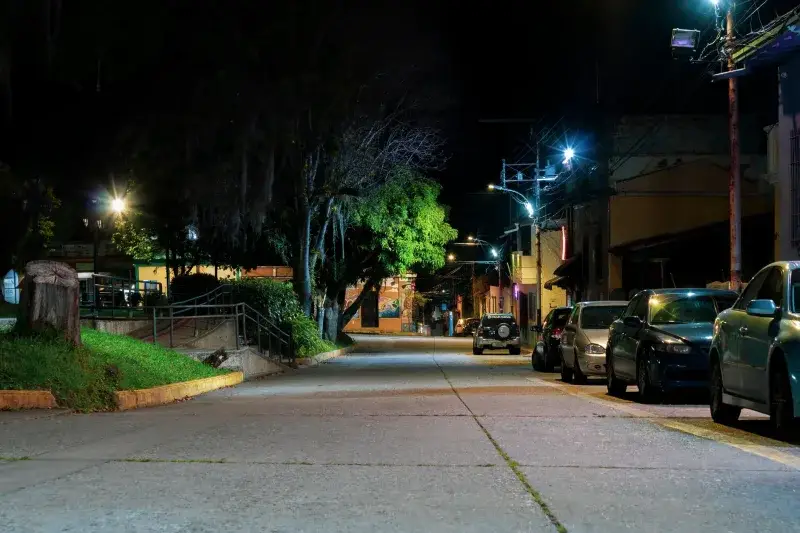 A serene nighttime street scene in Mérida, Venezuela, with parked cars and glowing streetlights.