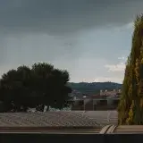 A view of Valencia's urban landscape with cypress trees and rain clouds hinting at an impending storm.