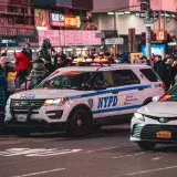 NYPD vehicle patrolling a busy city street in New York at night. Vibrant urban scene with city lights.