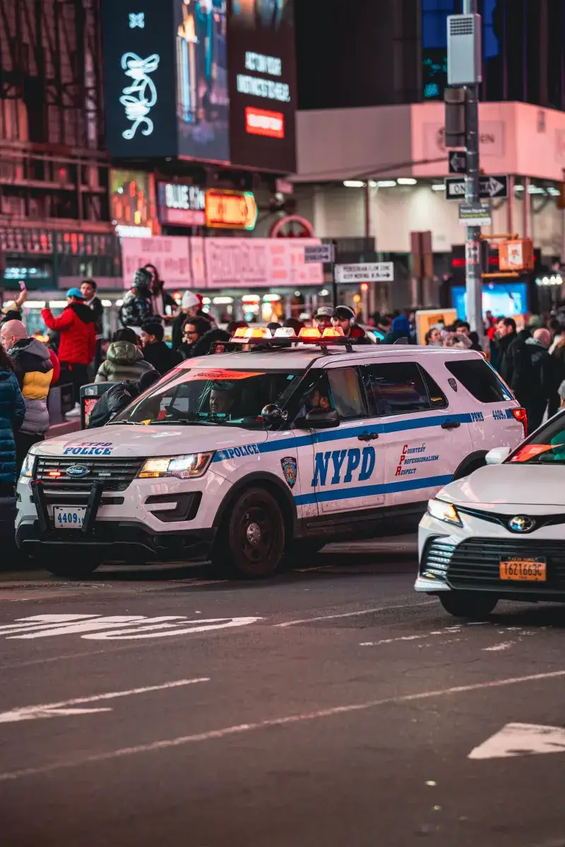 NYPD vehicle patrolling a busy city street in New York at night. Vibrant urban scene with city lights.