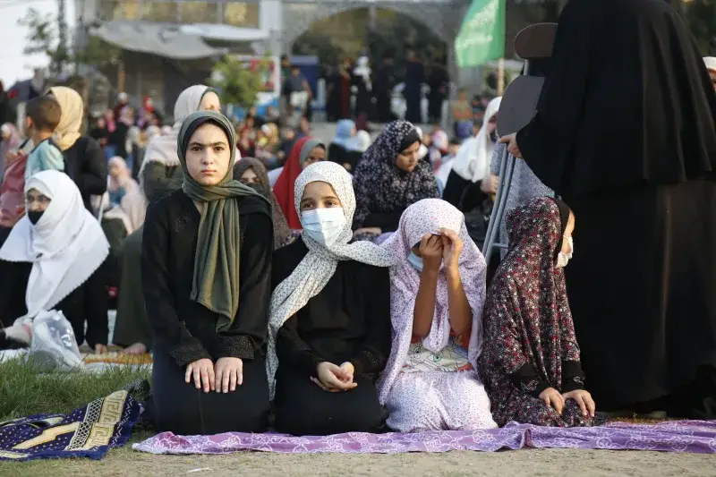 Mujeres musulmanas con hiyab se reúnen al aire libre para orar en Gaza, resaltando tradiciones culturales y religiosas.