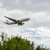 Un avión comercial volando sobre vegetación exuberante con cielos nublados en Barcelona, España.