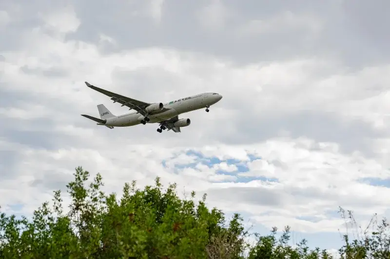 Un avión comercial volando sobre vegetación exuberante con cielos nublados en Barcelona, España.