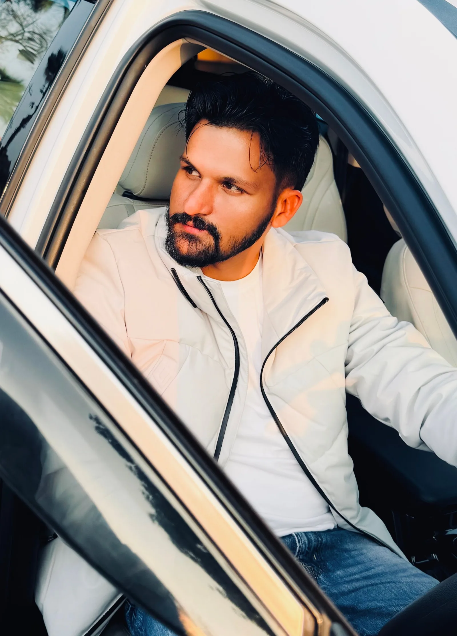 Bearded man in a white jacket sitting in a car, Khanna, India.