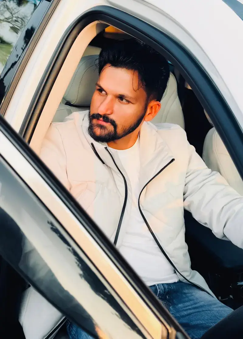 Bearded man in a white jacket sitting in a car, Khanna, India.