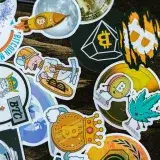 Colorful stickers featuring Bitcoin and cryptocurrency themes on a wooden surface.