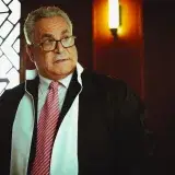 A male judge in a courtroom in Baghdad wearing a robe and tie, in a contemplative pose.