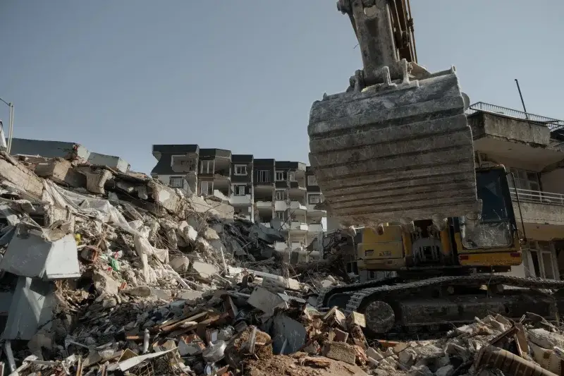 Powerful excavator clearing earthquake debris amidst building ruins in Antakya, Turkey.