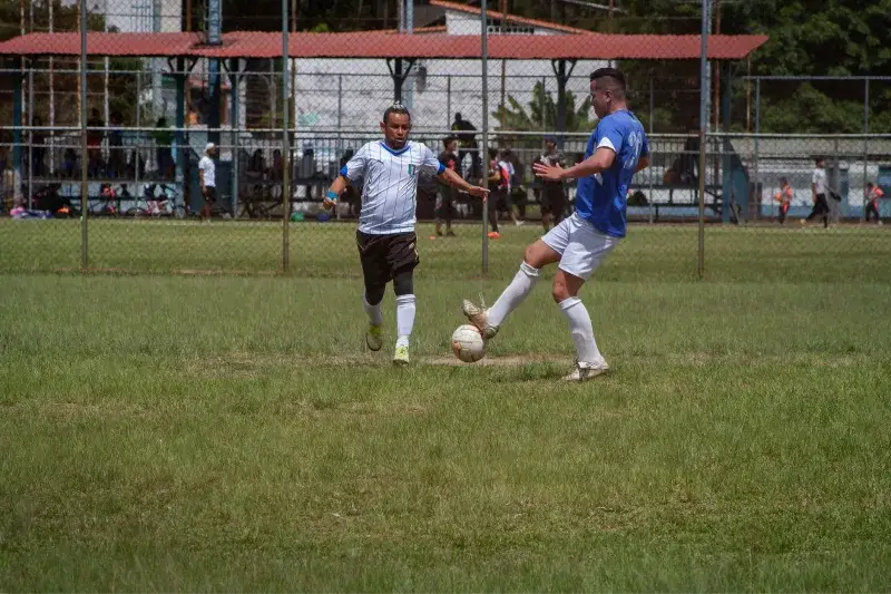 Two male soccer players competing in an outdoor match on a sunny day.
