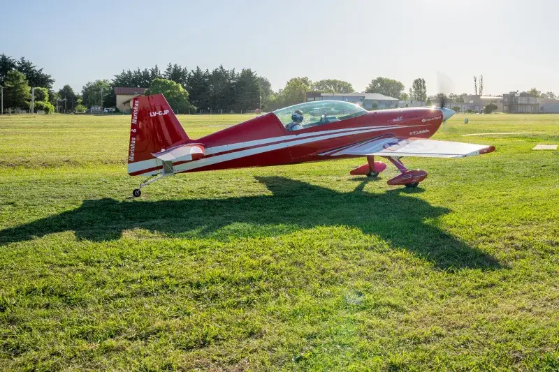A striking red aerobatic plane on a sunny day at General Rodríguez Airfield, Argentina.