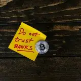 A conceptual image of a bitcoin coin next to a note that says 'Do not trust banks'.