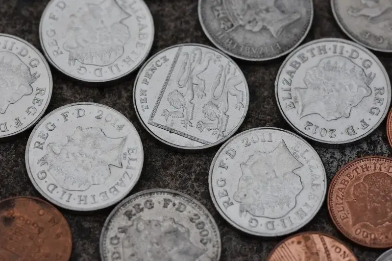 Close-up image of various British coins on a textured stone surface.