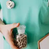 Anonymous crop man in light green medical uniform with stethoscope standing with clipboard and holding vial with drug in clinic