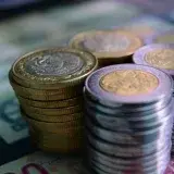 Close-up of stacked gold and silver coins on various currency notes, symbolizing wealth and savings.