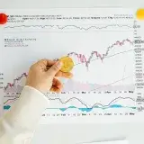 A hand holding a Bitcoin coin in front of a stock market chart, symbolizing analysis and finance.