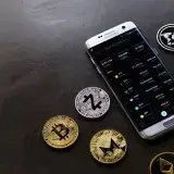 A collection of cryptocurrency coins and a smartphone displaying a digital trading platform.