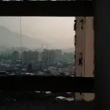 A dramatic urban view of Caracas with buildings framed by a window, casting shadows in the cityscape.