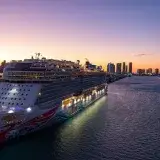A luxury cruise ship docked in Miami Bay at sunset with city skyline views.