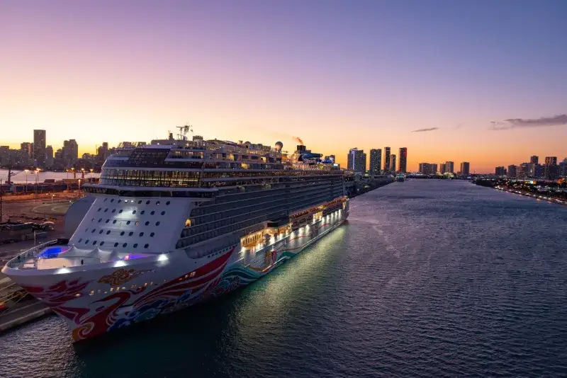 A luxury cruise ship docked in Miami Bay at sunset with city skyline views.
