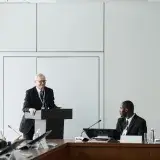 Formal business meeting with a diverse group and speaker at a podium in a conference room.