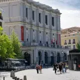 Vista diurna del Teatro Real en Madrid, con personas paseando, bajo cielos despejados.