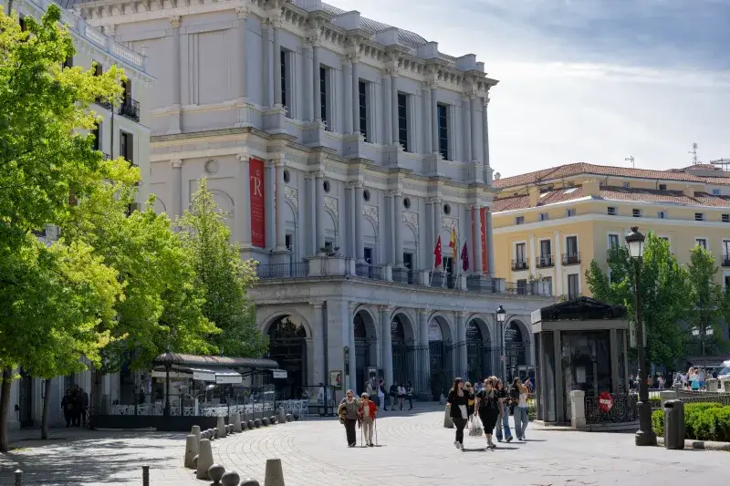 Vista diurna del Teatro Real en Madrid, con personas paseando, bajo cielos despejados.
