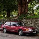 Vintage Saab 900 parked on an urban street in Keswick, UK, beside a stone wall and cemetery.