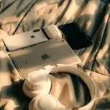 Unacolección de dispositivos Apple que incluye MacBook, iPad y iPhone en una cama con luz solar.