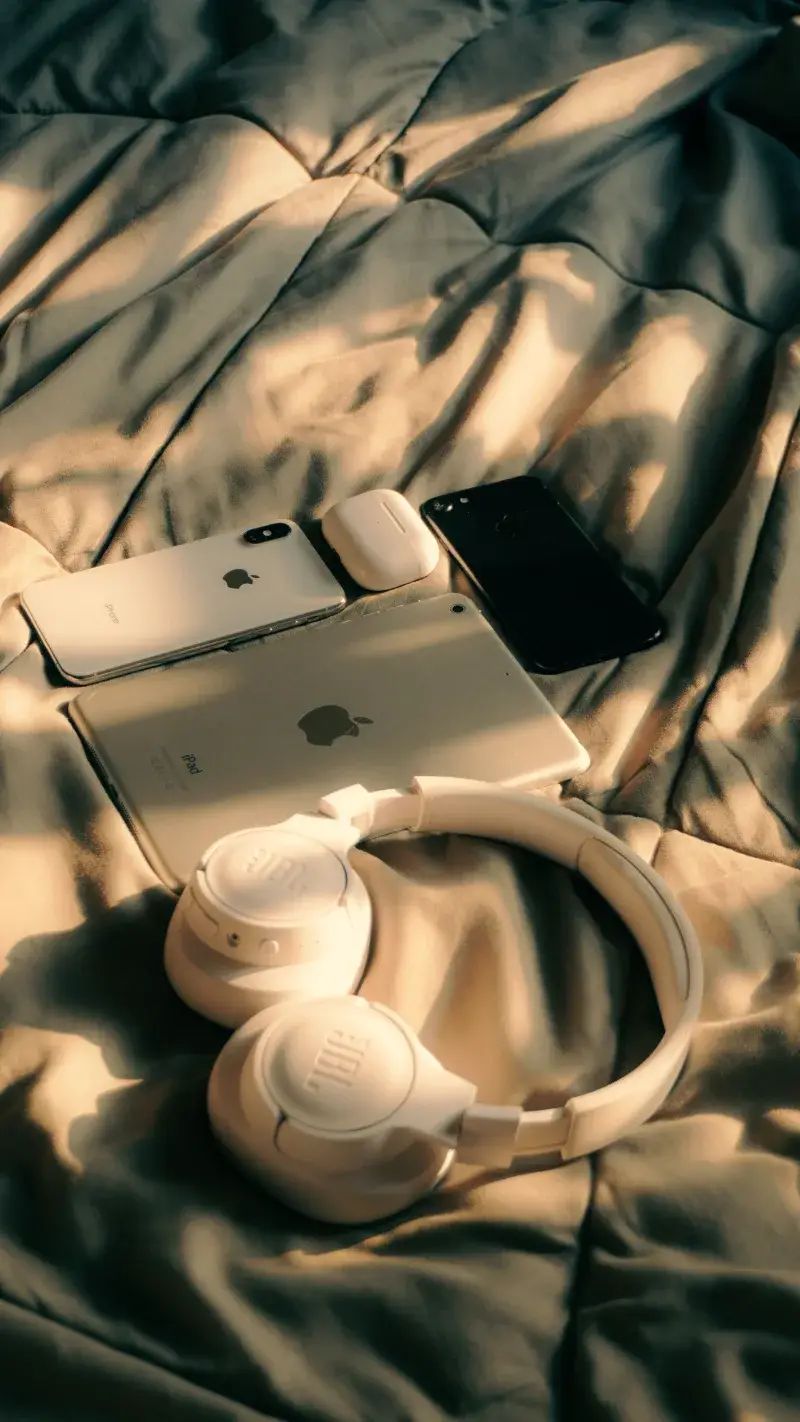 Unacolección de dispositivos Apple que incluye MacBook, iPad y iPhone en una cama con luz solar.