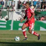 Soccer player in red uniform dribbling a ball during a match on a sunny day.