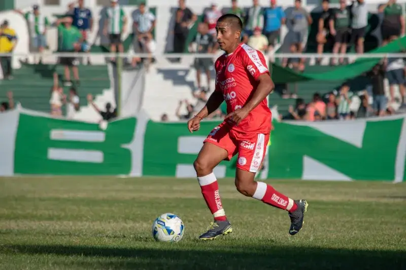 Soccer player in red uniform dribbling a ball during a match on a sunny day.