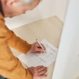 Senior man marking a ballot at a voting booth in an indoor polling station.