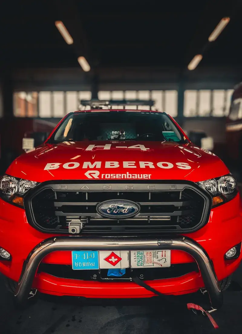 Front view of a red fire truck with 'Bomberos' displayed, parked indoors.
